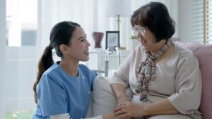 An elderly person and adult family member unpacking boxes together in a sunny, furnished bedroom.